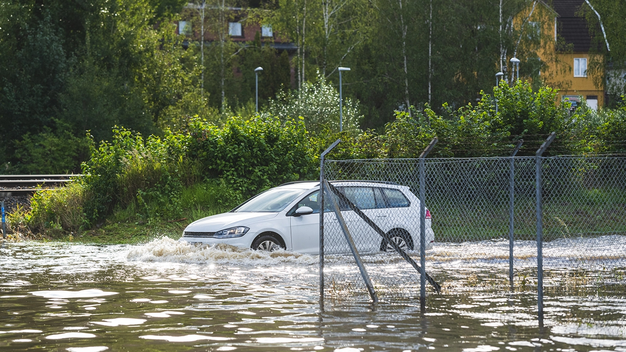 En personbil kör genom ett översvämmat område, där vattennivån når upp längs bilens sidor.