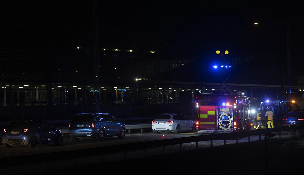 Nattlig trafikolycka på en motorväg med flera bilar och en brandbil med blåljus tända. Räddningspersonal arbetar vid vägkanten.