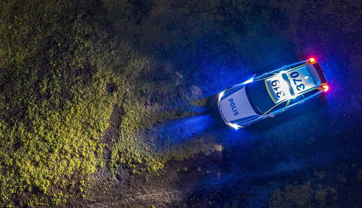Polisbil sedd uppifrån i mörker med blå och röda ljus som lyser upp marken runt fordonet.