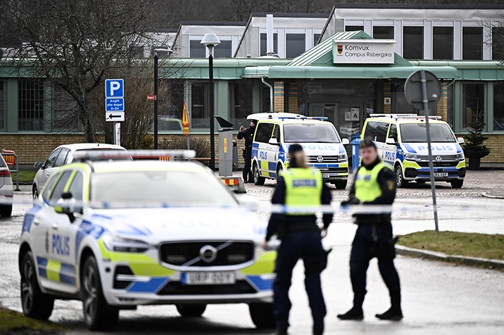 Polisbilar och uniformerade poliser står utanför en skolbyggnad i en avspärrad utemiljö.