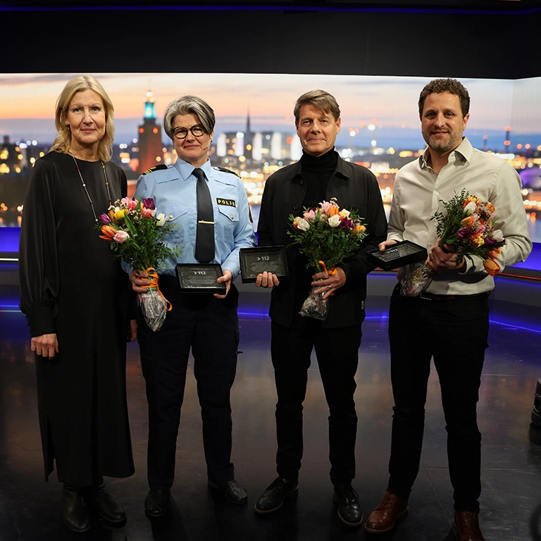 Fyra personer står på en scen i en studio och håller blombuketter och priser i händerna.
