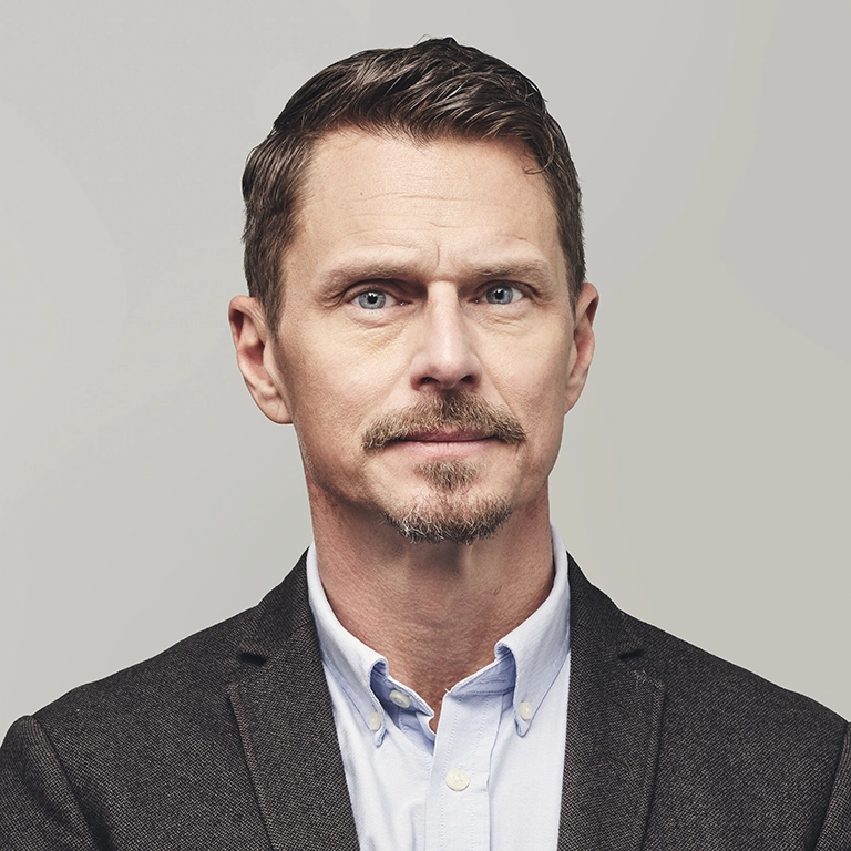 Person i kavaj och skjorta fotograferad mot en ljus bakgrund.