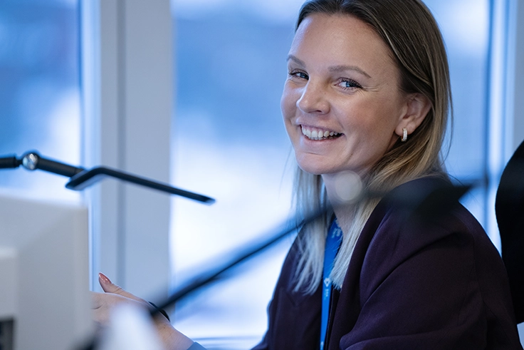 Kvinna som sitter framför sin dator och ler in i kamera.