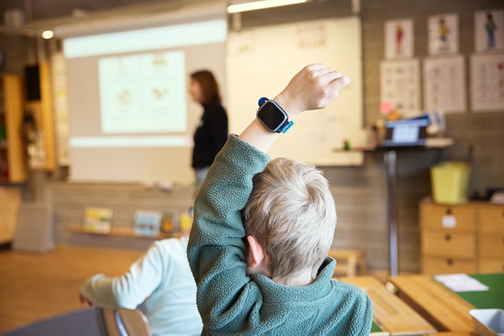 Barn med smart klocka räcker upp handen i klassrum